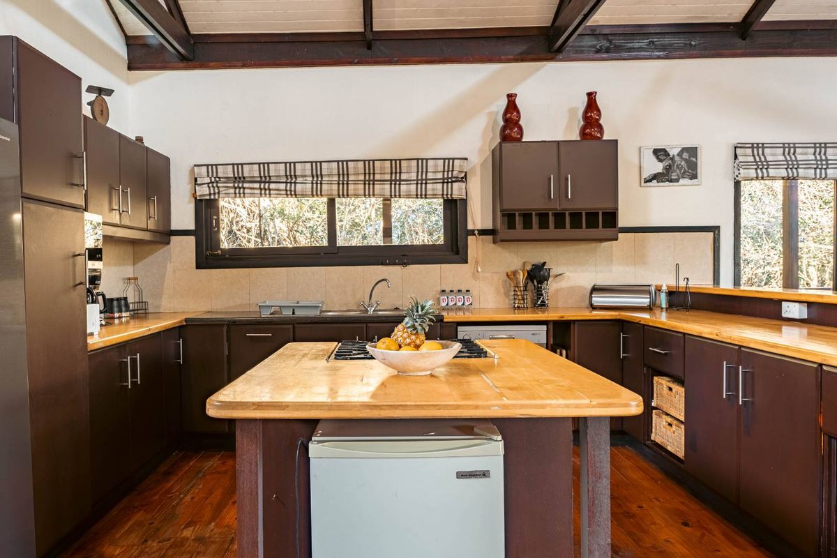 A rustic kitchen featuring dark cabinetry, a central wooden island with a built-in cooktop, and exposed timber ceiling beams.