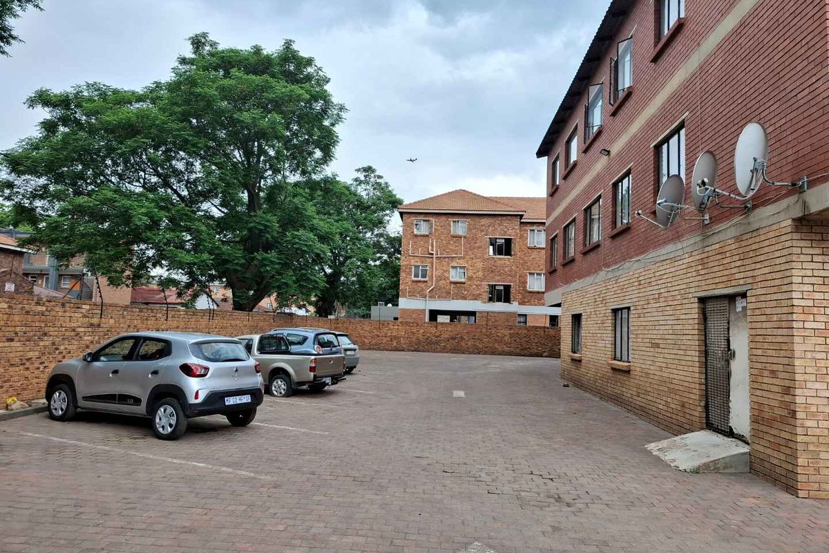 Exterior view of the apartment complex featuring a paved parking area, brick facade, and perimeter boundary wall.