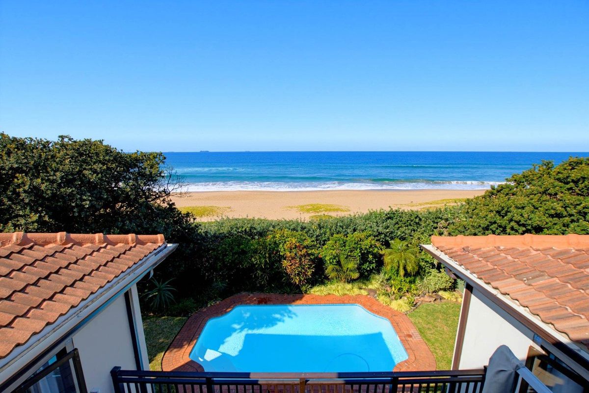 Elevated view overlooking a private swimming pool with direct beach and ocean access, framed by established coastal vegetation.