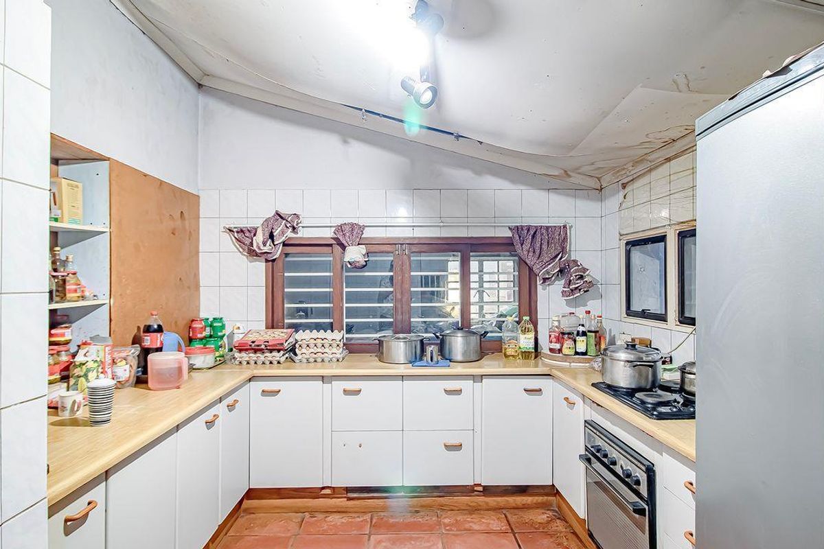 A dated kitchen featuring U-shaped cabinetry, a built-in oven and hob, and tiled flooring, requiring cosmetic updates and ceiling repairs.