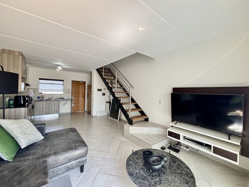 Open-plan living area featuring a modern staircase with stainless steel balustrades, tiled flooring, and an integrated kitchen space.