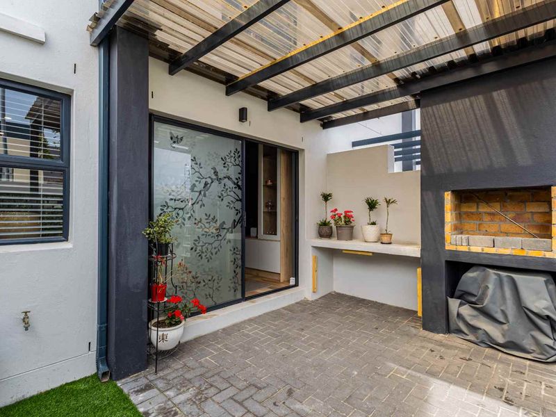 Covered patio area featuring a built-in brick braai, concrete prep counter, and sliding glass door access to the interior living space.