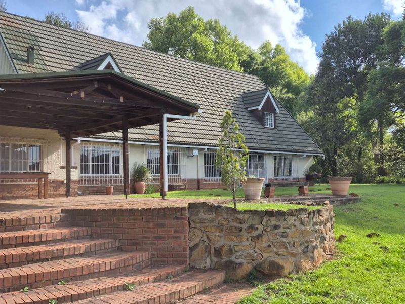 Rear view of the house featuring a spacious brick patio, timber pergola, and stone retaining wall set against a large garden.