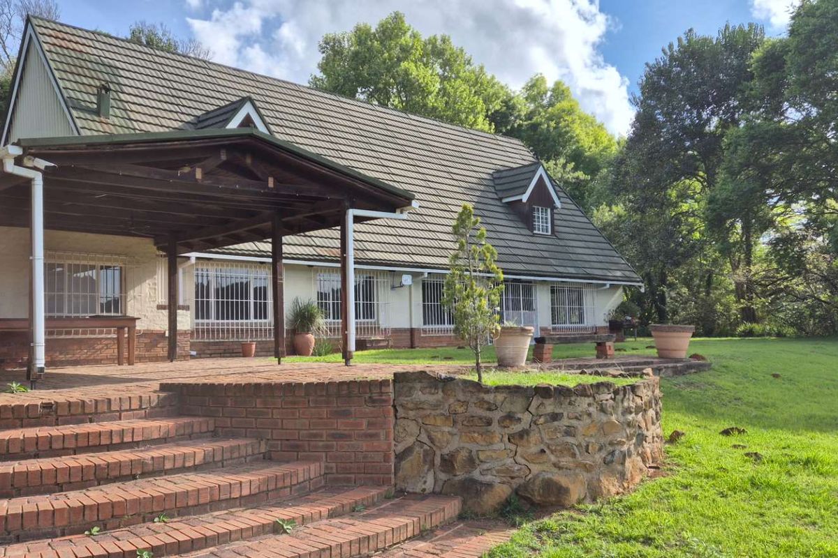 Rear view of the house featuring a spacious brick patio, timber pergola, and stone retaining wall set against a large garden.