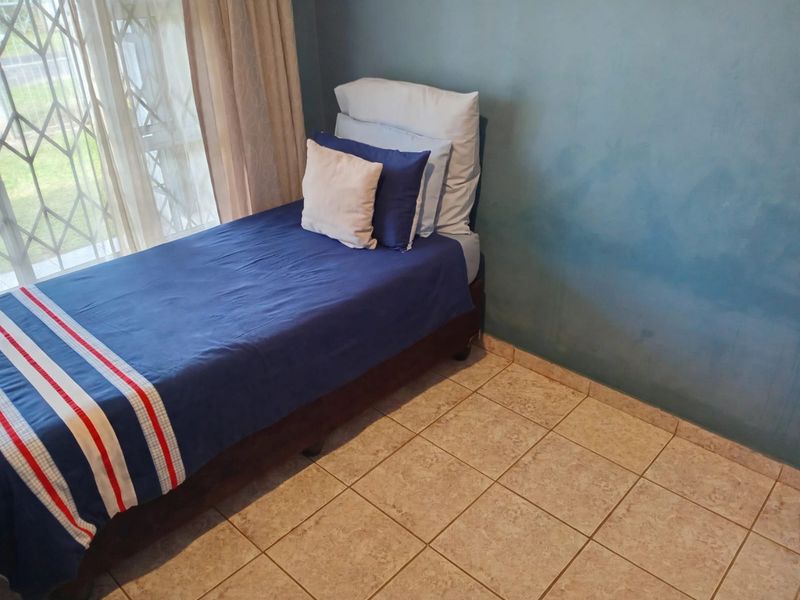 A bedroom featuring tiled flooring and a security gate on the window, with blue painted walls.