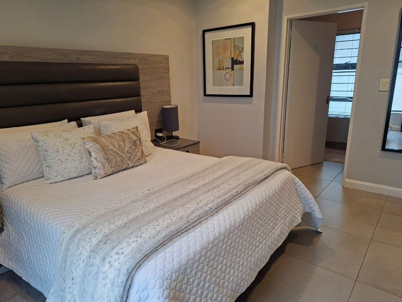 A well-maintained bedroom featuring neutral tiled flooring, a modern built-in headboard, and direct access to an adjoining room.