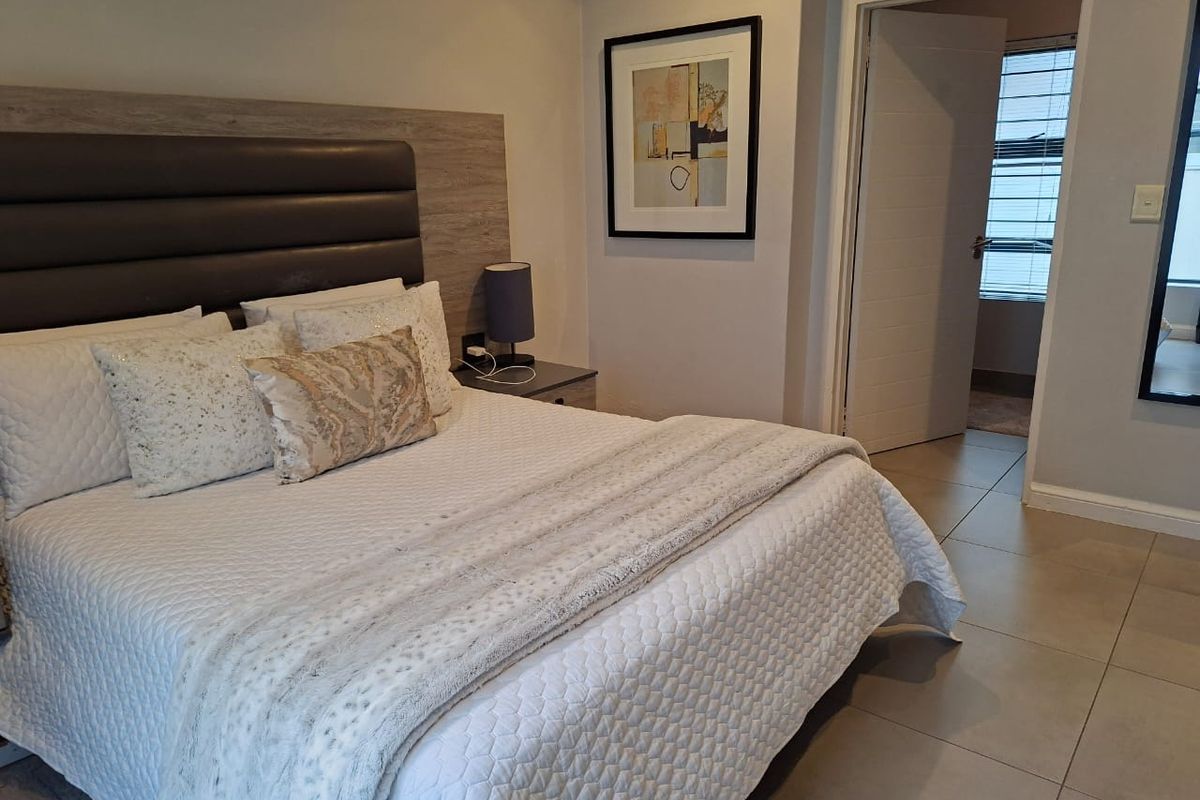 A well-maintained bedroom featuring neutral tiled flooring, a modern built-in headboard, and direct access to an adjoining room.