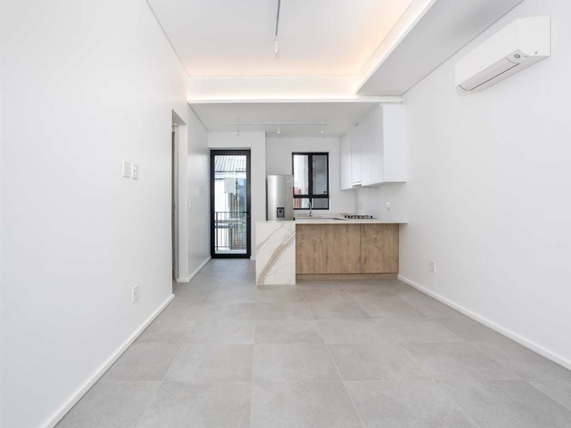 Modern open-plan kitchen and living area featuring sleek cabinetry, stone countertops, tiled flooring, and a wall-mounted air conditioning unit.