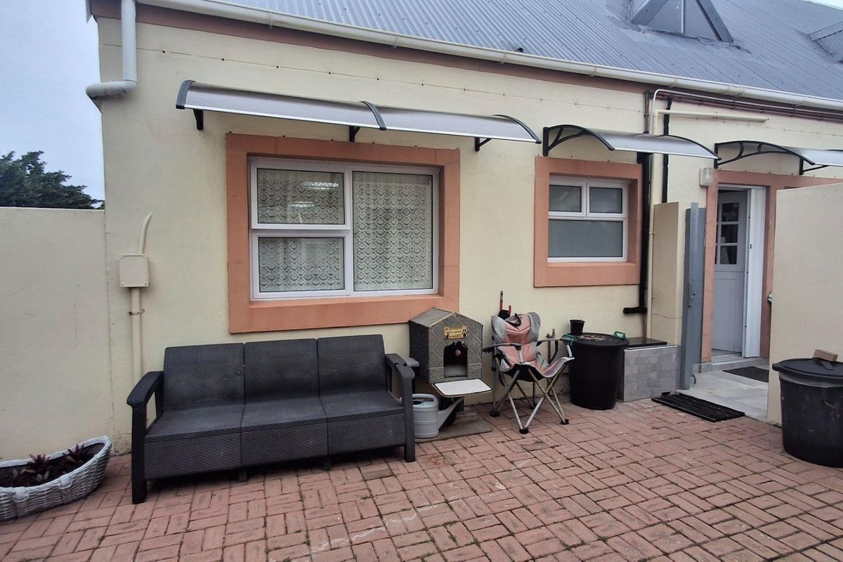 Rear exterior view of the apartment featuring a paved patio area, protective awnings over windows, and access to the main entrance.