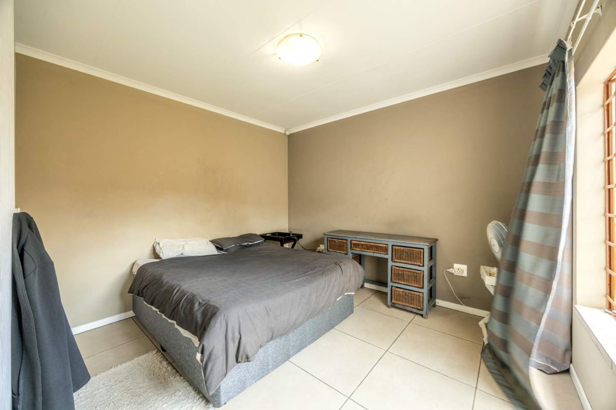 A functional bedroom featuring neutral tiled flooring, painted walls, and a window fitted with security bars.