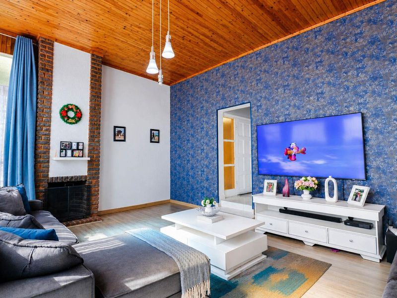 A cozy living room featuring a prominent exposed brick fireplace, warm timber ceiling, and striking blue textured wallpaper.