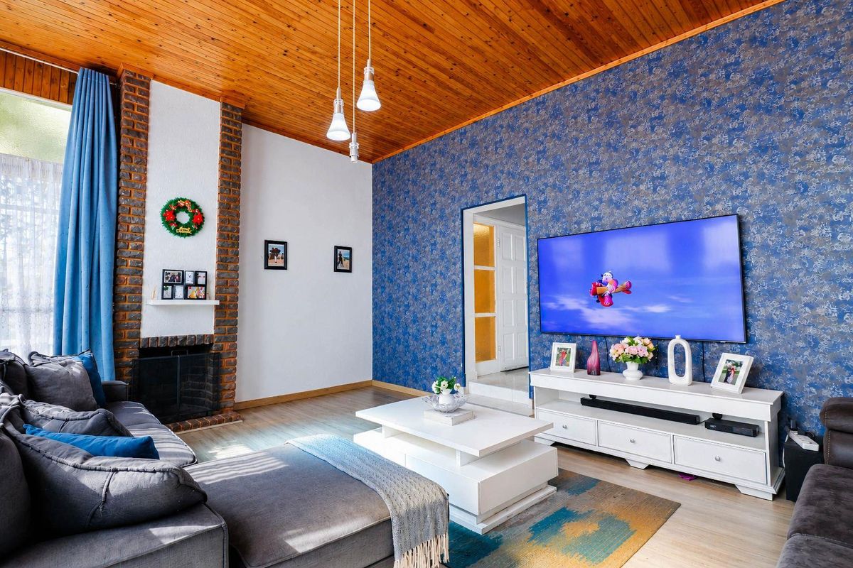 A cozy living room featuring a prominent exposed brick fireplace, warm timber ceiling, and striking blue textured wallpaper.