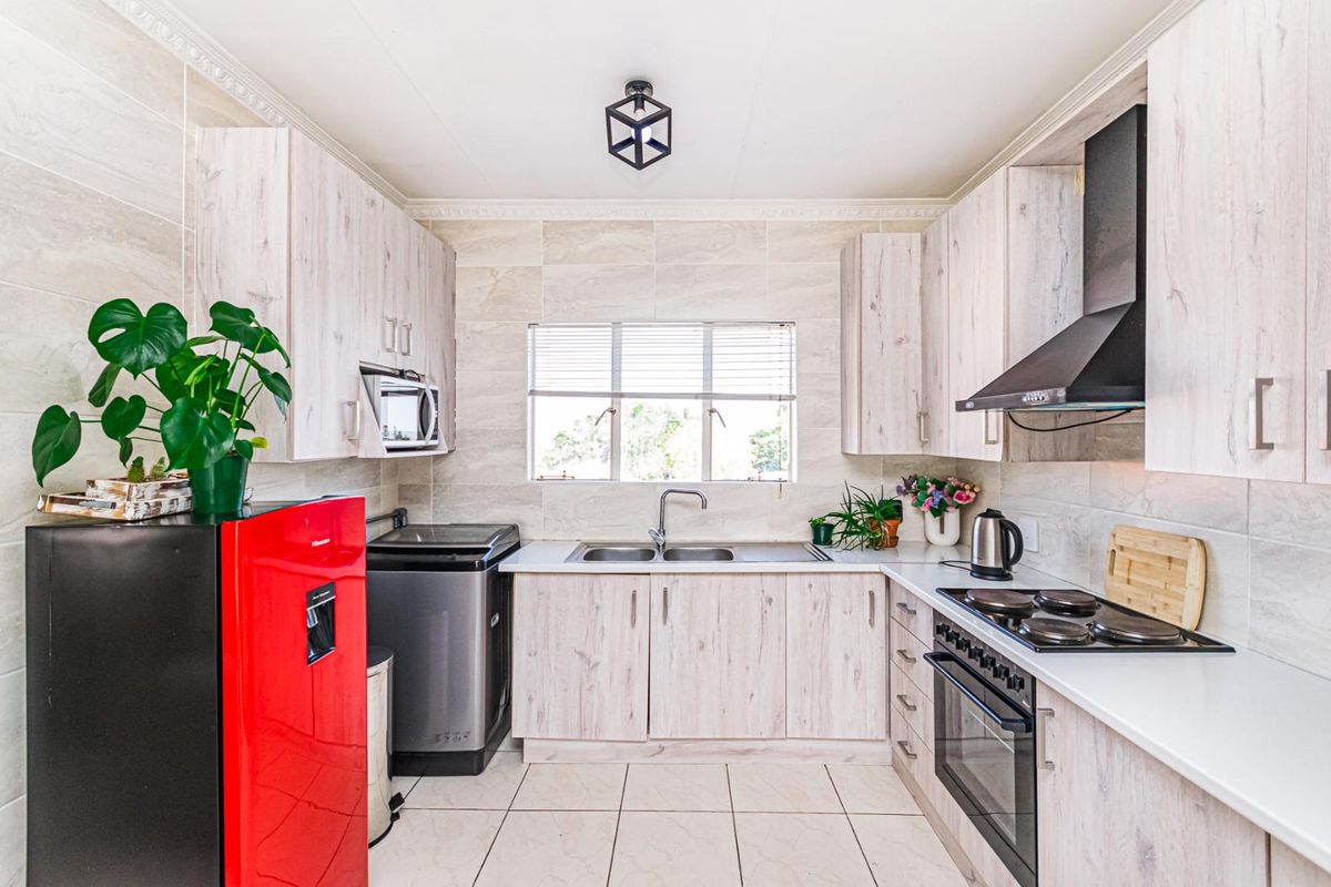 Modern kitchen featuring light wood-grain cabinetry, stone-look wall tiles, built-in oven, hob, extractor fan, and double stainless steel sink.