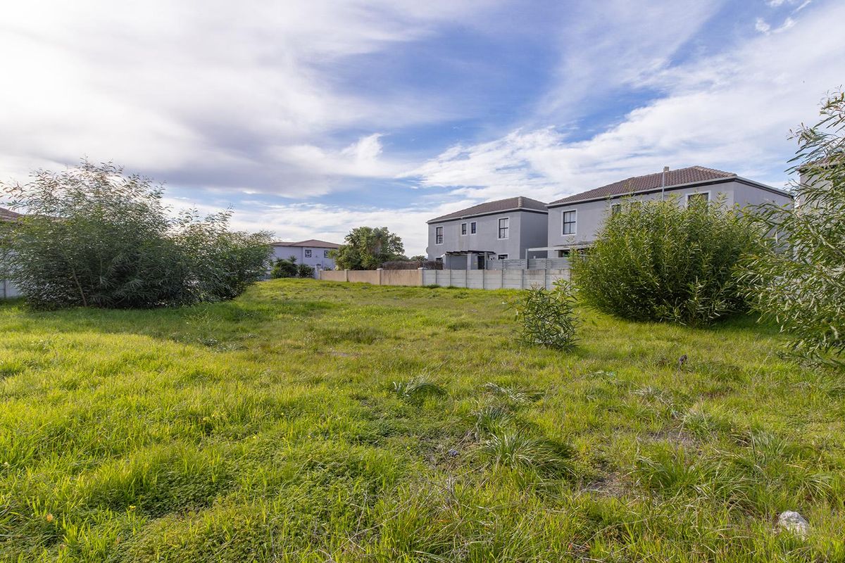 A vacant residential plot featuring natural grass coverage and enclosed by precast concrete boundary walls in a suburban setting.