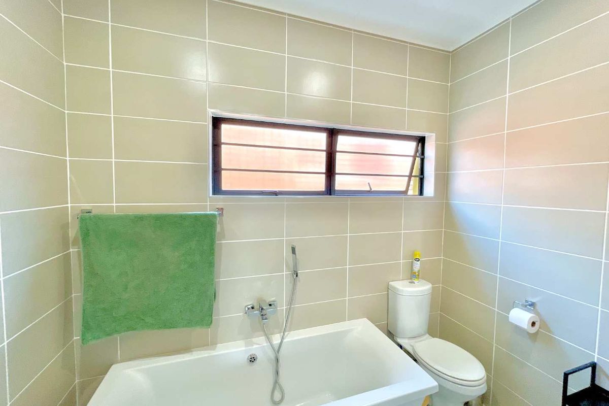 A clean, functional bathroom featuring full-height wall tiling, a built-in bathtub with handheld shower mixer, and a standard toilet.