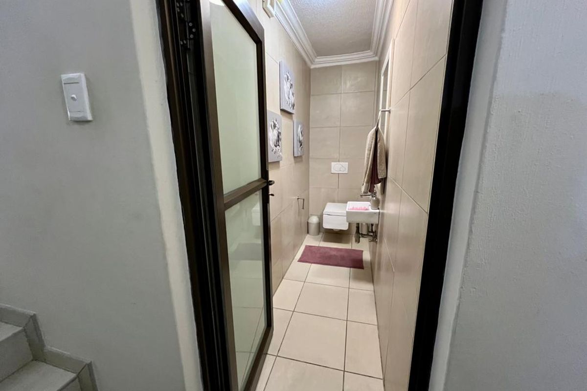 A compact guest bathroom featuring wall-mounted toilet, small basin, and neutral floor-to-ceiling tiling.