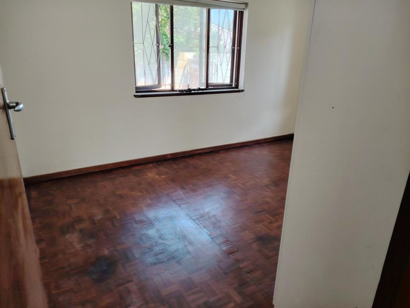 An empty bedroom featuring original parquet flooring, timber window frames with security bars, and neutral wall finishes.