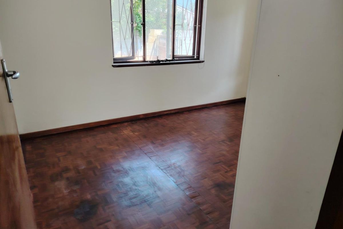 An empty bedroom featuring original parquet flooring, timber window frames with security bars, and neutral wall finishes.
