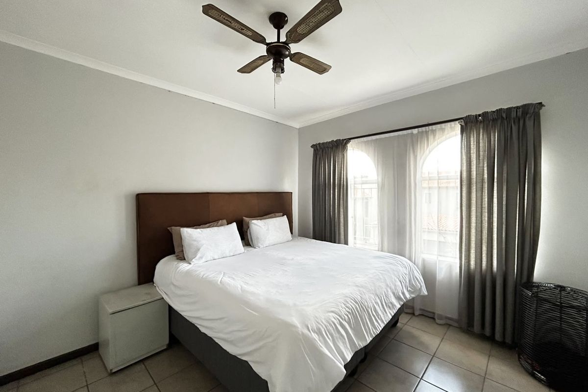 A well-lit bedroom featuring tiled flooring, a ceiling fan, and distinctive arched windows that allow for natural light.