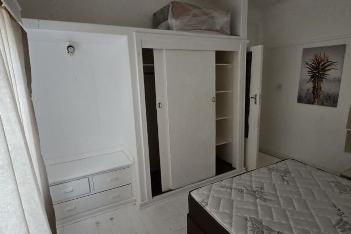 A bedroom featuring built-in sliding door wardrobes with integrated shelving and drawer storage units.
