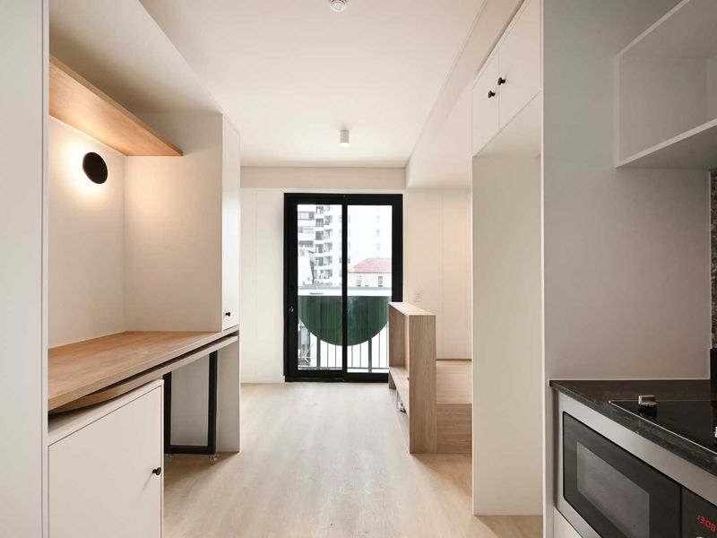 Modern open-plan apartment interior featuring a sleek kitchen with integrated appliances, built-in cabinetry, and a bright living area with access to a balcony.