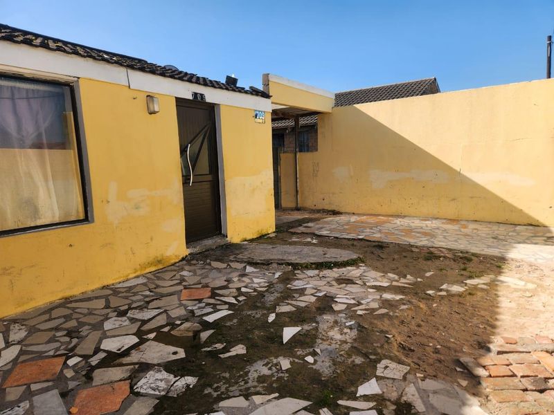 Rear exterior view of the property featuring a paved courtyard area, boundary walls, and access to the main structure.