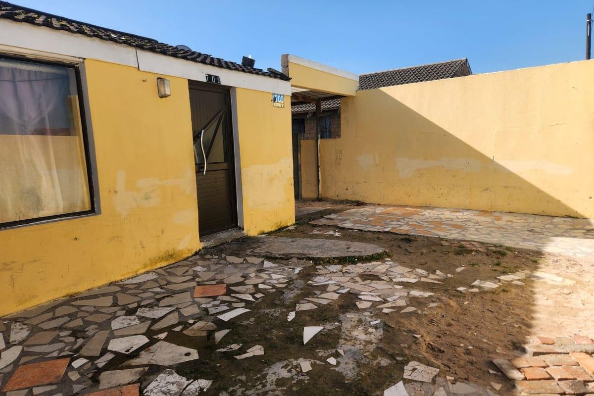 Rear exterior view of the property featuring a paved courtyard area, boundary walls, and access to the main structure.