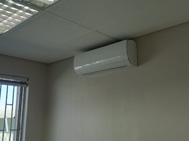 A clean, empty office space featuring a suspended ceiling with recessed lighting and a wall-mounted air conditioning unit.