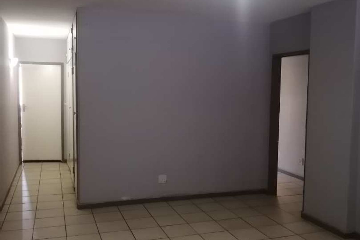An empty living area featuring neutral ceramic floor tiles and access to adjacent rooms through internal doorways.