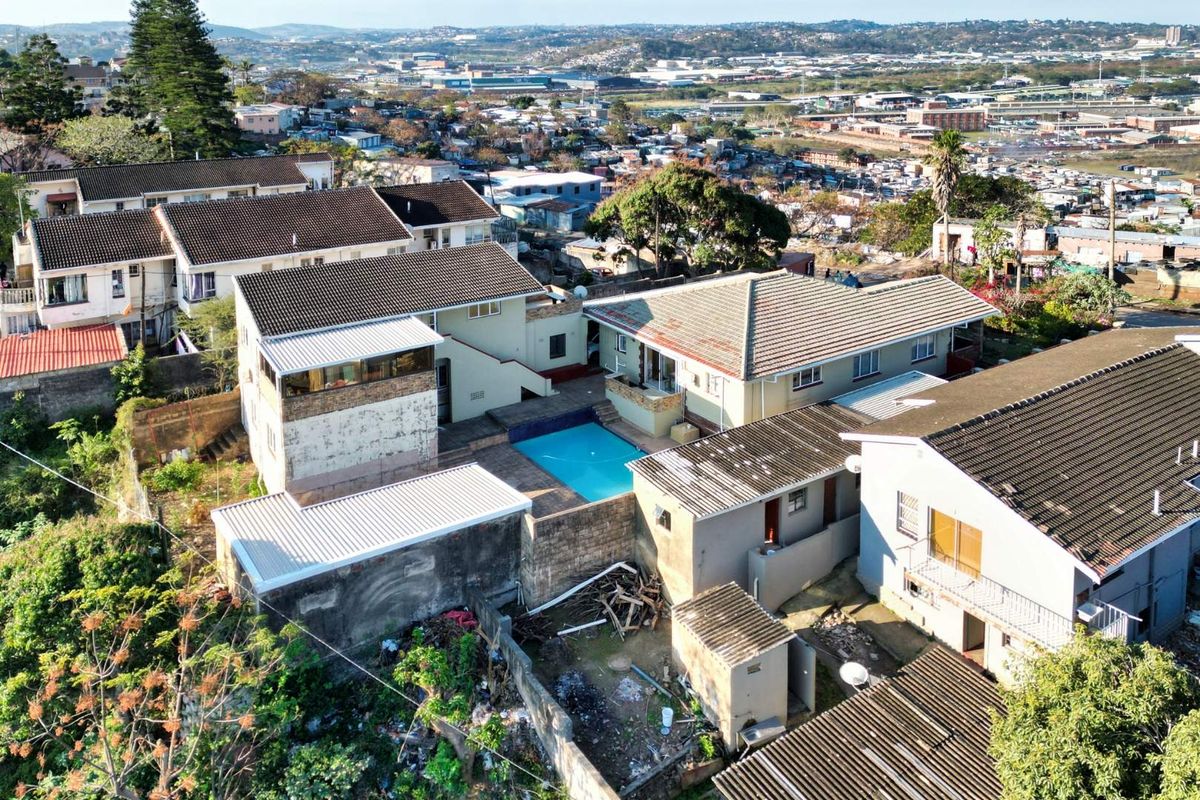 Aerial view of a residential property featuring a swimming pool, multiple roof structures, and surrounding yard space in a dense urban setting.