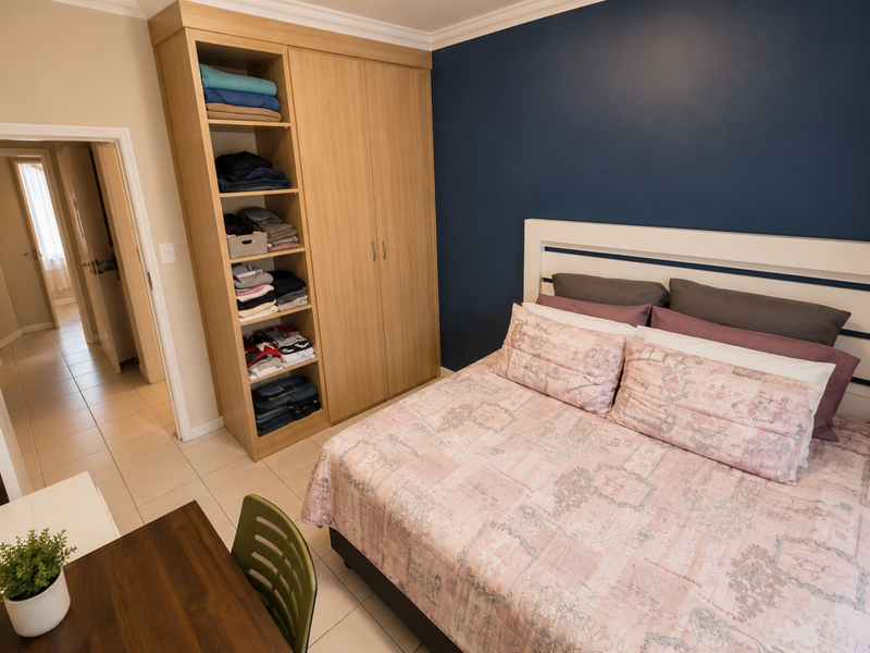 A well-maintained bedroom featuring a built-in wooden wardrobe, tiled flooring, and a bold navy accent wall.