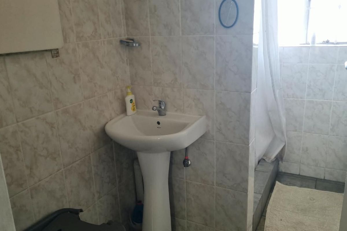 A functional bathroom featuring a pedestal basin and a shower area with tiled walls, requiring cosmetic updates to improve its overall condition.