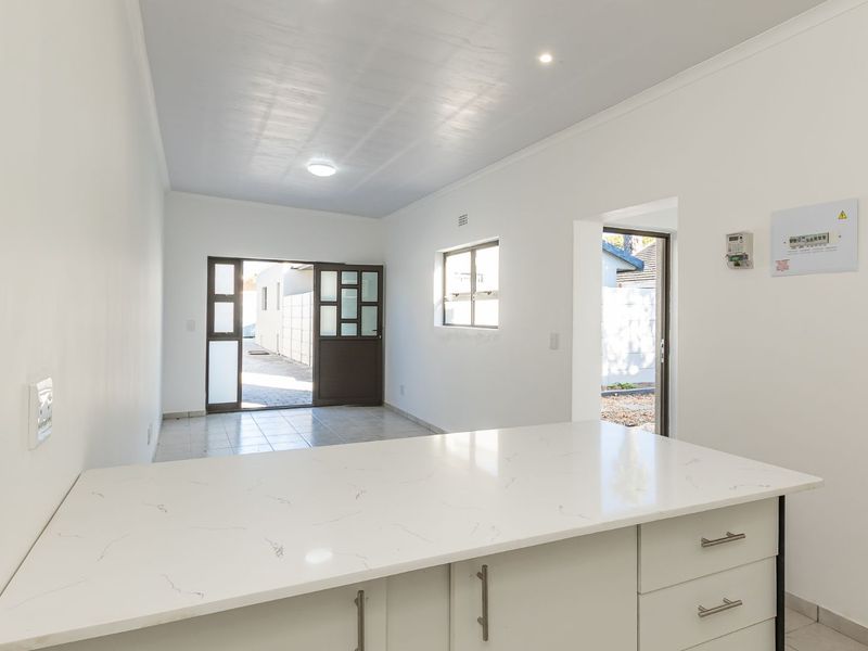 Bright open-plan living area featuring a modern kitchen island with quartz countertops, tiled flooring, and direct access to the exterior.