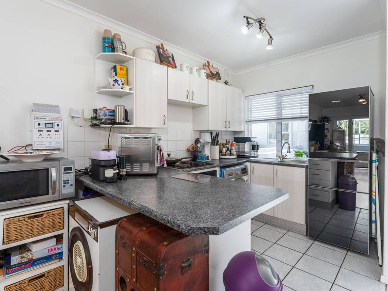 A functional kitchen featuring laminate cabinetry, stone-look countertops, tiled flooring, and a stainless steel sink with a modern mixer tap.