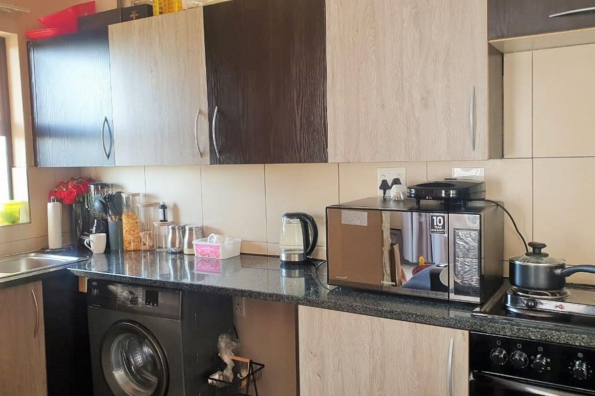 A functional kitchen featuring granite countertops, built-in cabinetry, a stainless steel oven with hob, and an integrated space for a washing machine.