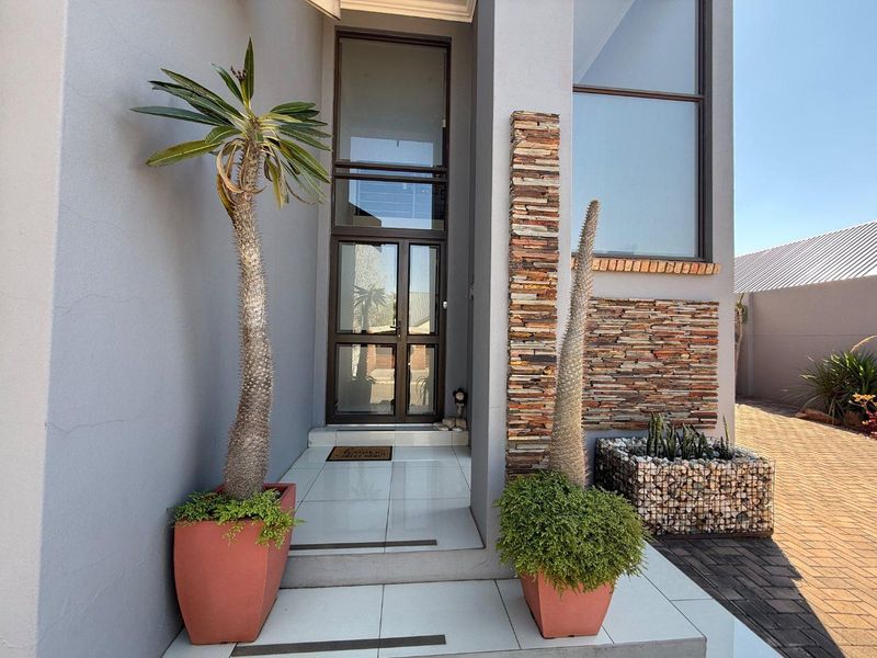 Modern front entrance featuring stacked stone feature wall, tiled steps, and a tall glass-panelled front door with large fixed window.