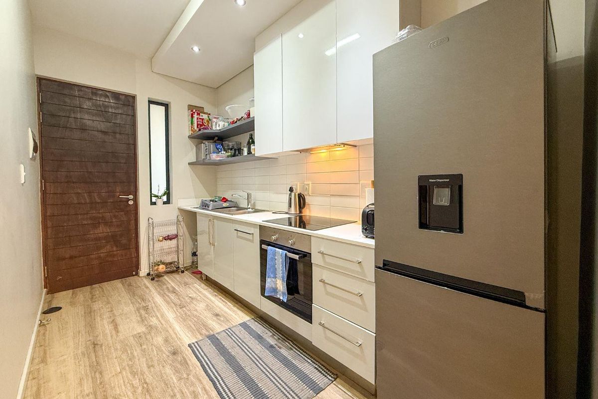 Modern kitchen featuring sleek white cabinetry, integrated appliances, electric hob, oven, and durable laminate flooring with efficient under-cabinet lighting.