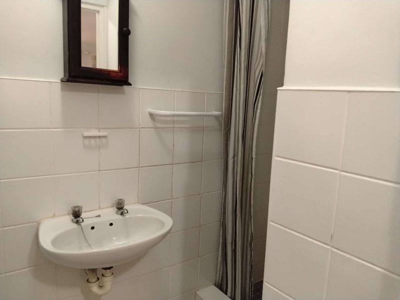 A functional bathroom featuring a wall-mounted basin and tiled walls, currently presenting in a dated condition.