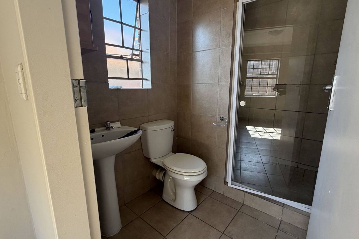 A functional bathroom featuring a pedestal basin, a standard toilet, and a glass-enclosed shower with neutral wall and floor tiling.