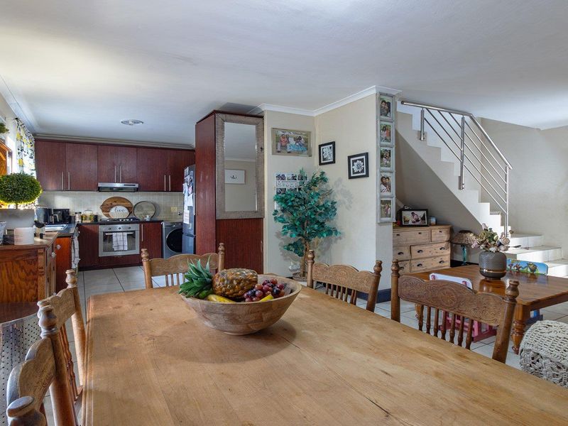 Open-plan living and dining area featuring a functional kitchen with built-in cabinetry and a staircase with a modern stainless steel railing.