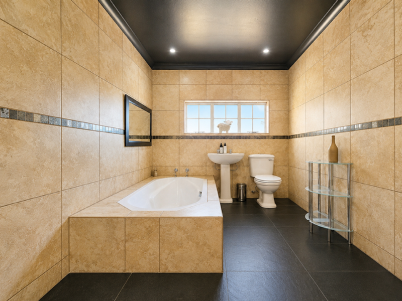 A well-maintained bathroom featuring a built-in bathtub, pedestal sink, toilet, and neutral floor-to-ceiling wall tiling with a dark contrasting ceiling.