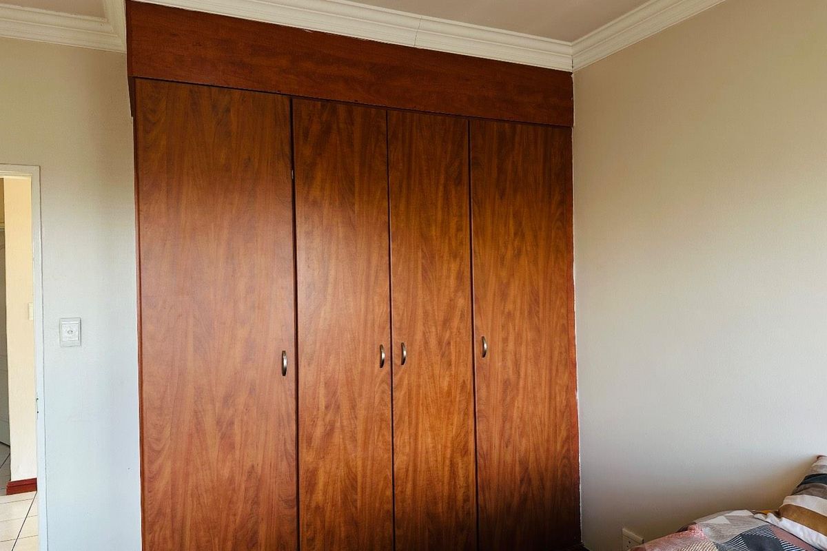 A bedroom featuring floor-to-ceiling built-in wooden wardrobes with integrated overhead storage and decorative crown molding.