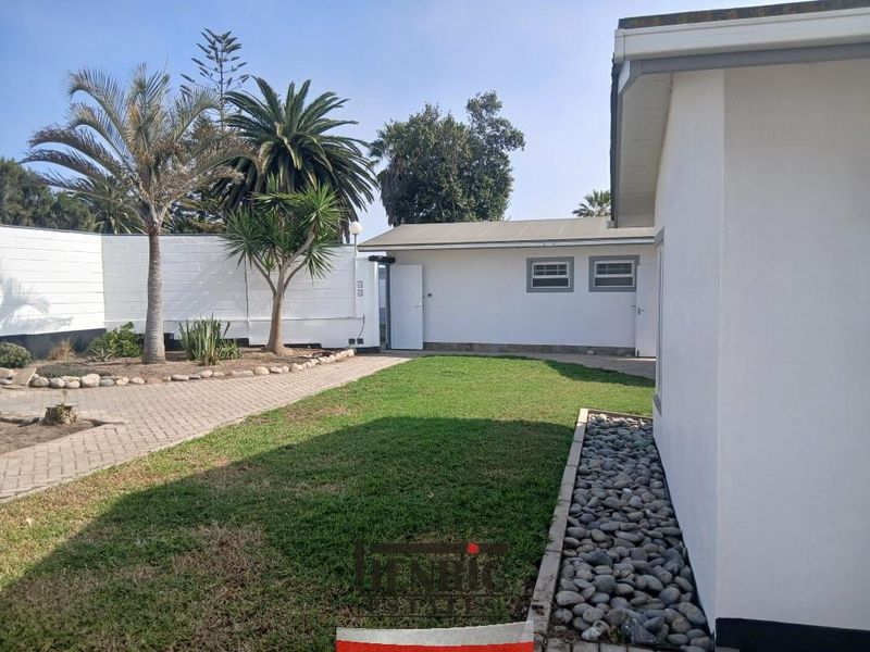A well-maintained rear exterior area featuring a paved driveway, a neat lawn, and a boundary wall.