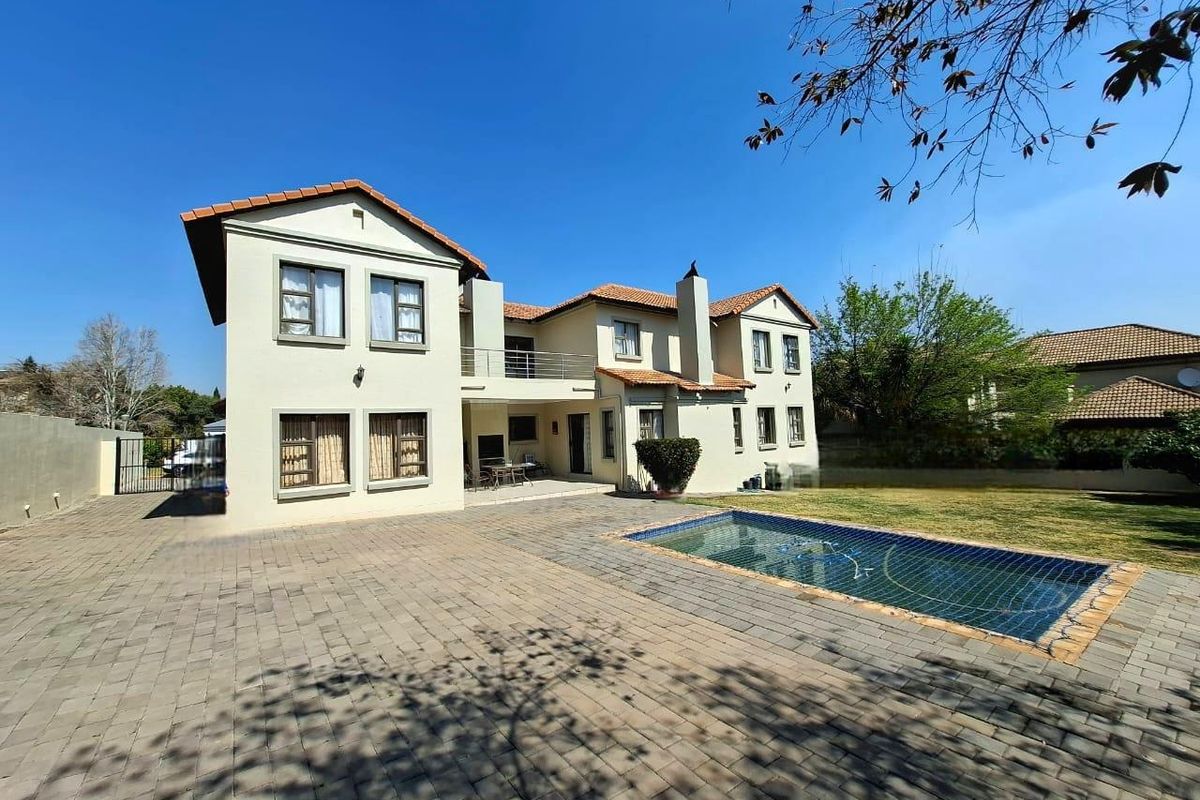 Rear view of a two-story house featuring a paved patio area, a swimming pool, and an upper-level balcony.