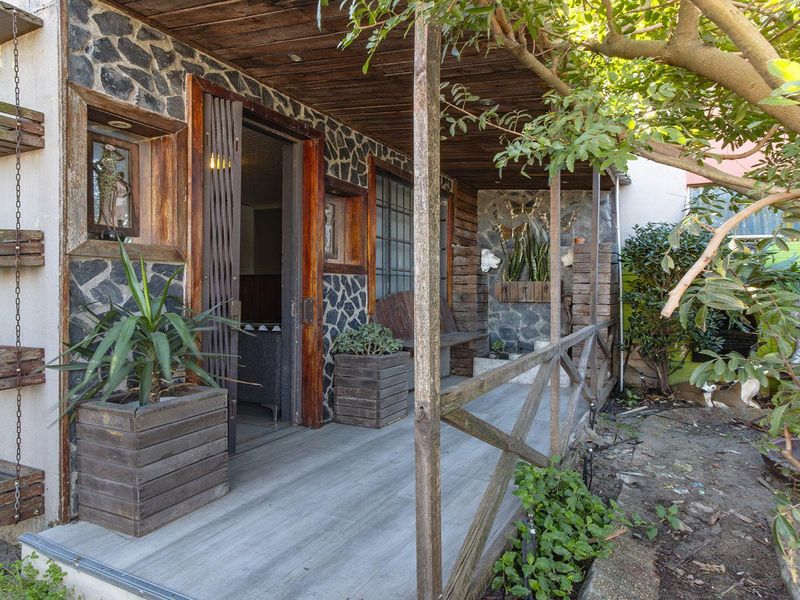 A rustic covered patio area featuring stone-clad walls, timber decking, and a wooden pergola, providing a sheltered outdoor transition space.