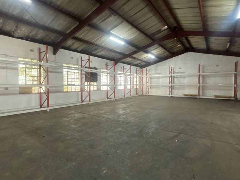 Spacious industrial warehouse unit featuring high ceilings with exposed steel trusses, concrete flooring, and extensive built-in steel racking systems for storage.