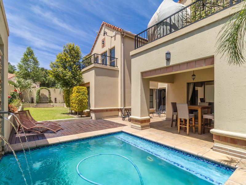 A well-maintained outdoor area featuring a swimming pool with a water feature, timber decking, and a covered patio space.
