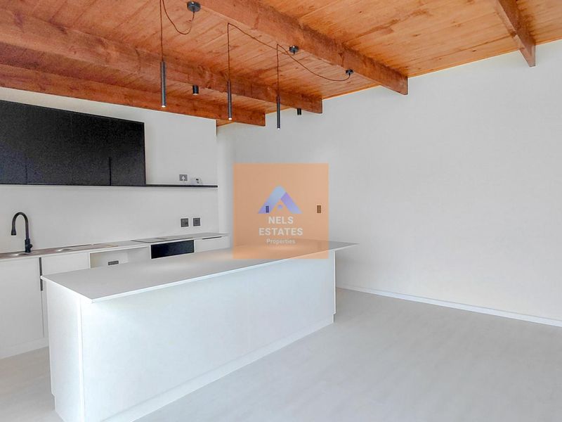Modern open-plan kitchen featuring a central island, sleek cabinetry, and striking exposed timber ceiling beams in a bright, minimalist space.