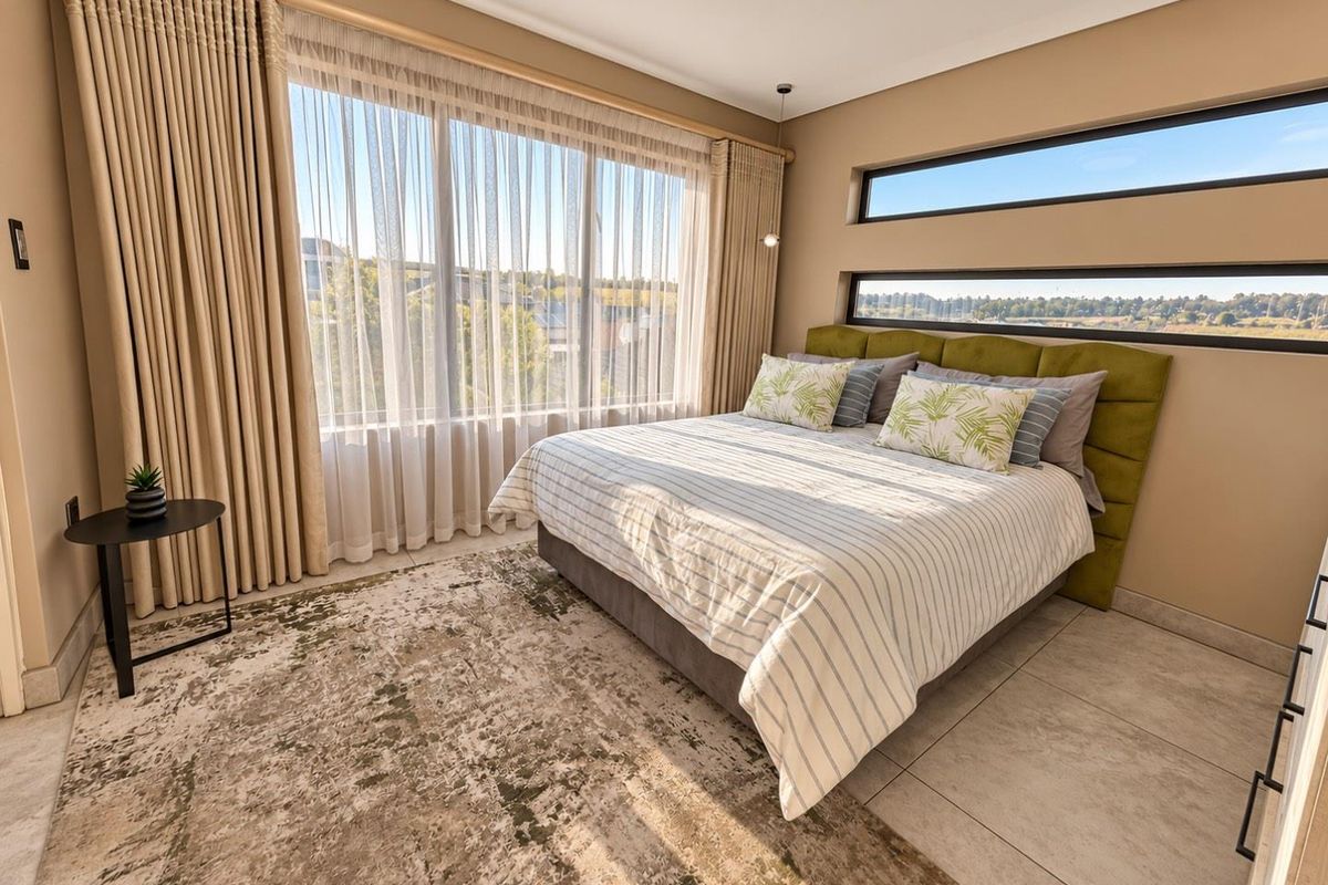 A modern, well-lit bedroom featuring large floor-to-ceiling windows, horizontal clerestory windows, and neutral tiled flooring.