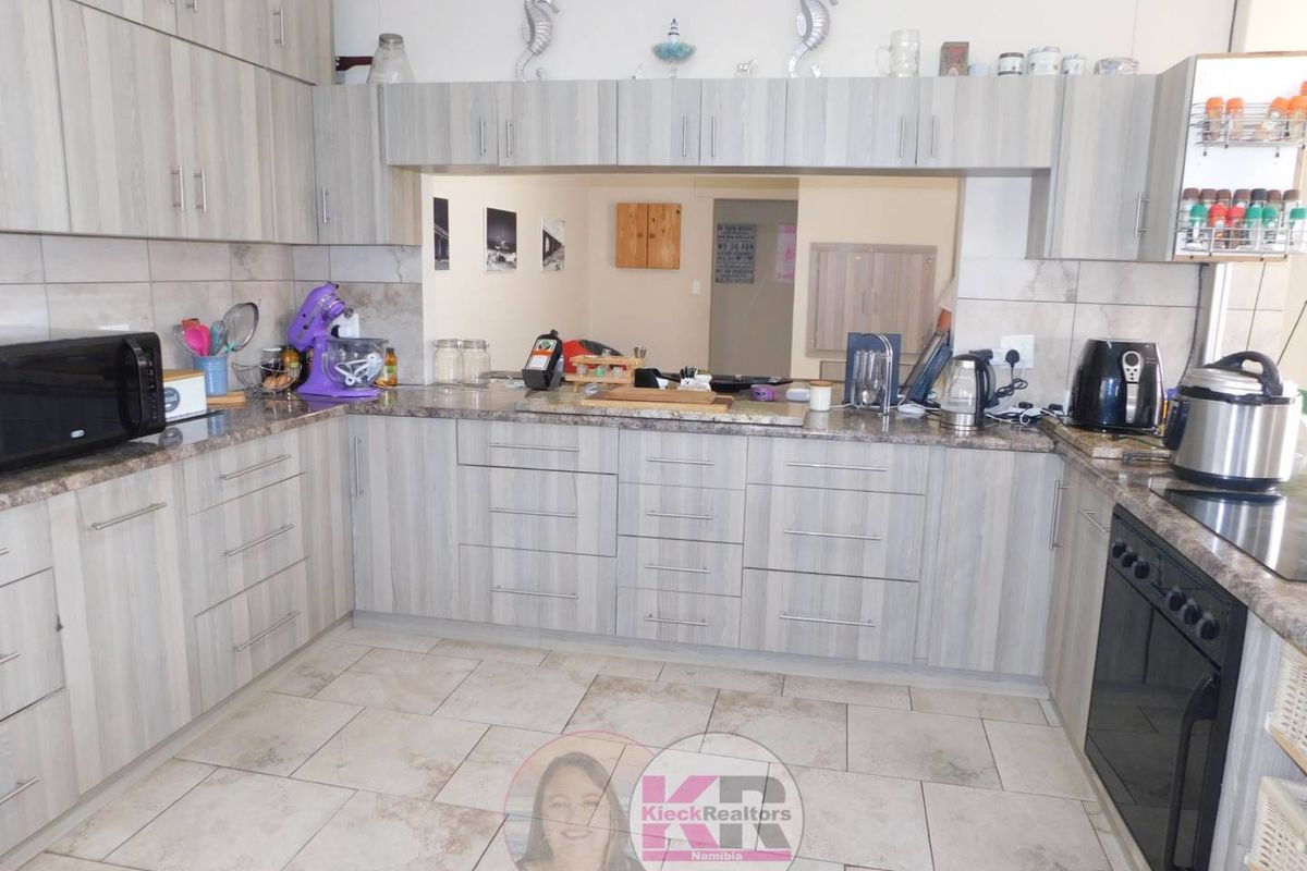 A functional kitchen featuring light wood-grain cabinetry, granite countertops, tiled flooring, and a convenient serving hatch opening to the adjacent living area.
